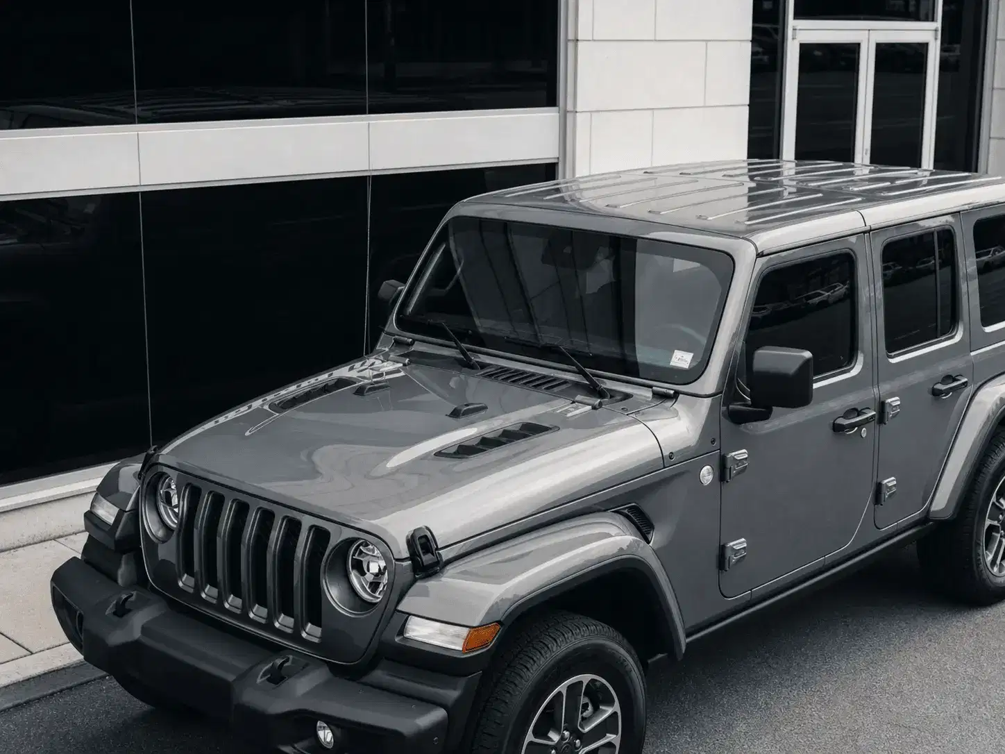 Incognito Tints finished gray Jeep Wrangler tint outside a shopfront with a blank white storefront panel